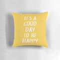 Bright yellow pillow with the text "It's a Good Day to Be Happy" in a fun, typographic design