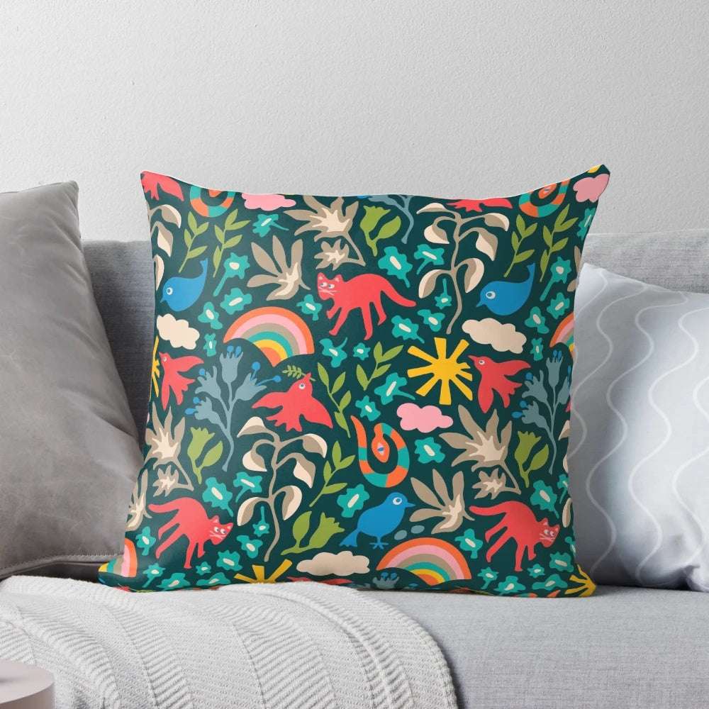 A colorful, nature-themed decorative pillow featuring birds, animals, flowers, rainbows, and clouds on a dark teal background.