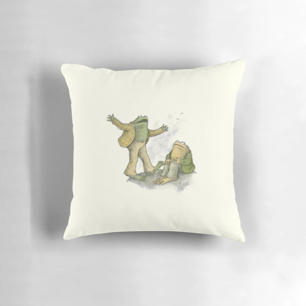 A soft, plush pillow featuring an illustration of two whimsical frogs and toads in a natural setting.