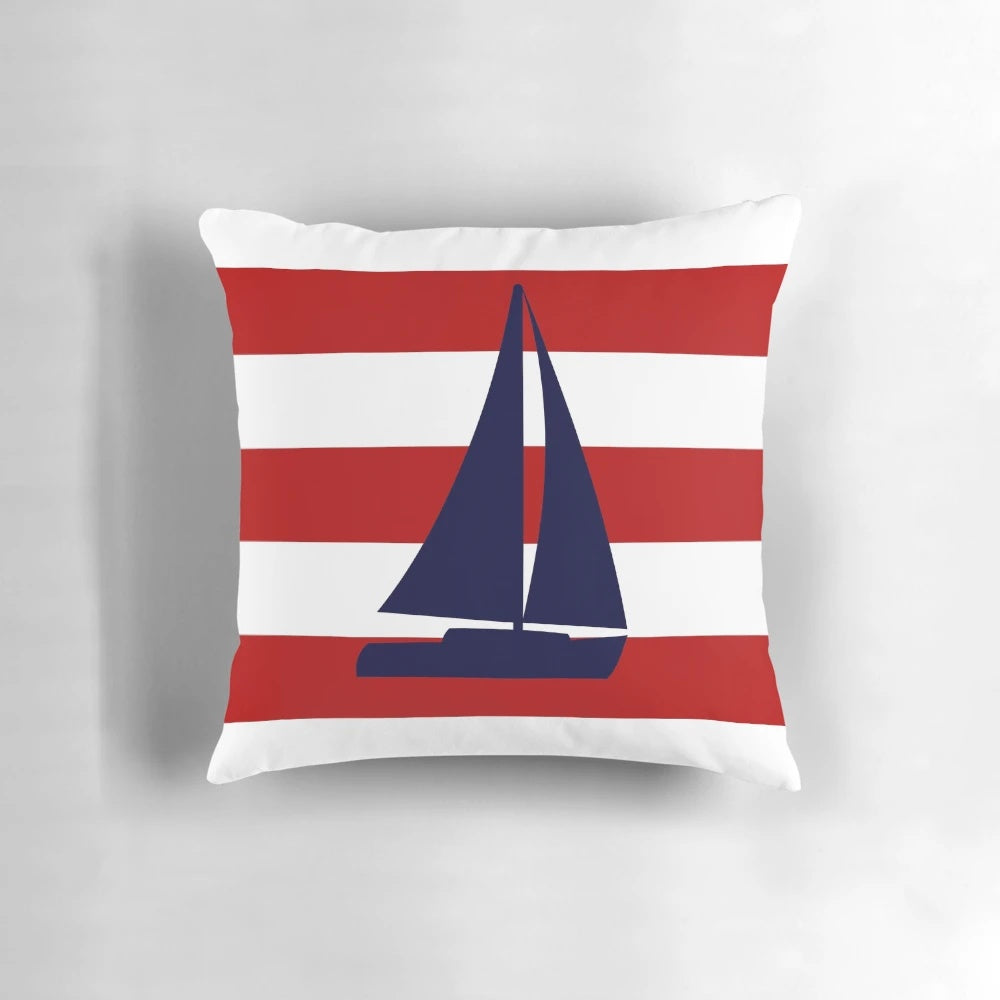 A navy blue pillow featuring a sailboat design against red and white striped background