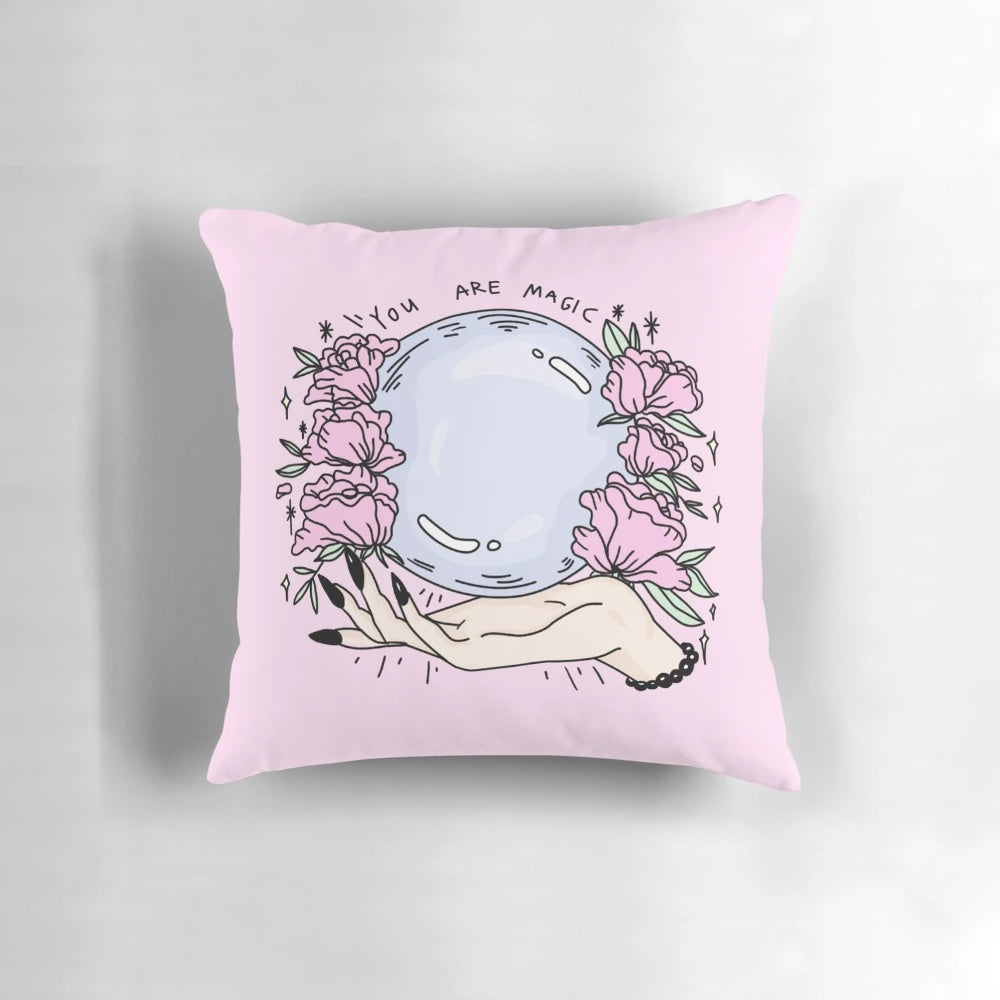 A pastel pink pillow featuring a beautiful floral design, with a touch of mystical elements like a crystal ball, perfect for creating a cozy and whimsical atmosphere.
