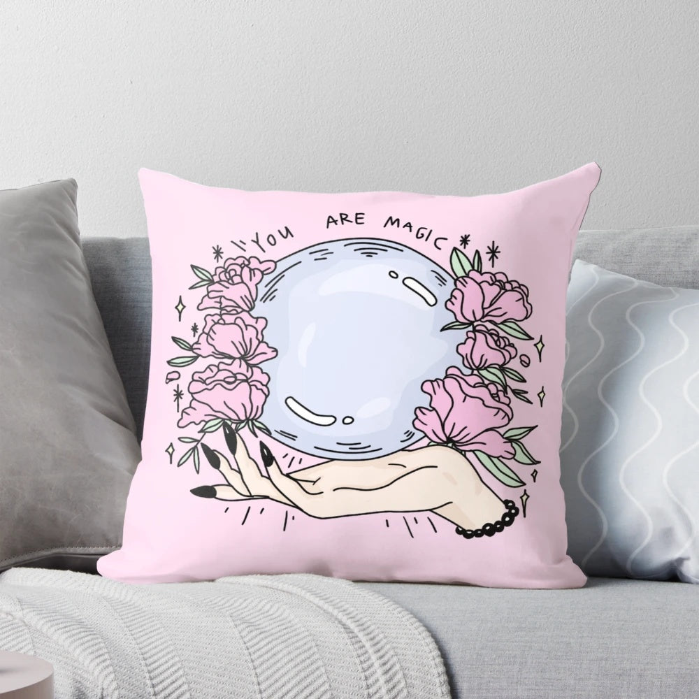A pastel pink pillow featuring a beautiful floral design, with a touch of mystical elements like a crystal ball, perfect for creating a cozy and whimsical atmosphere.