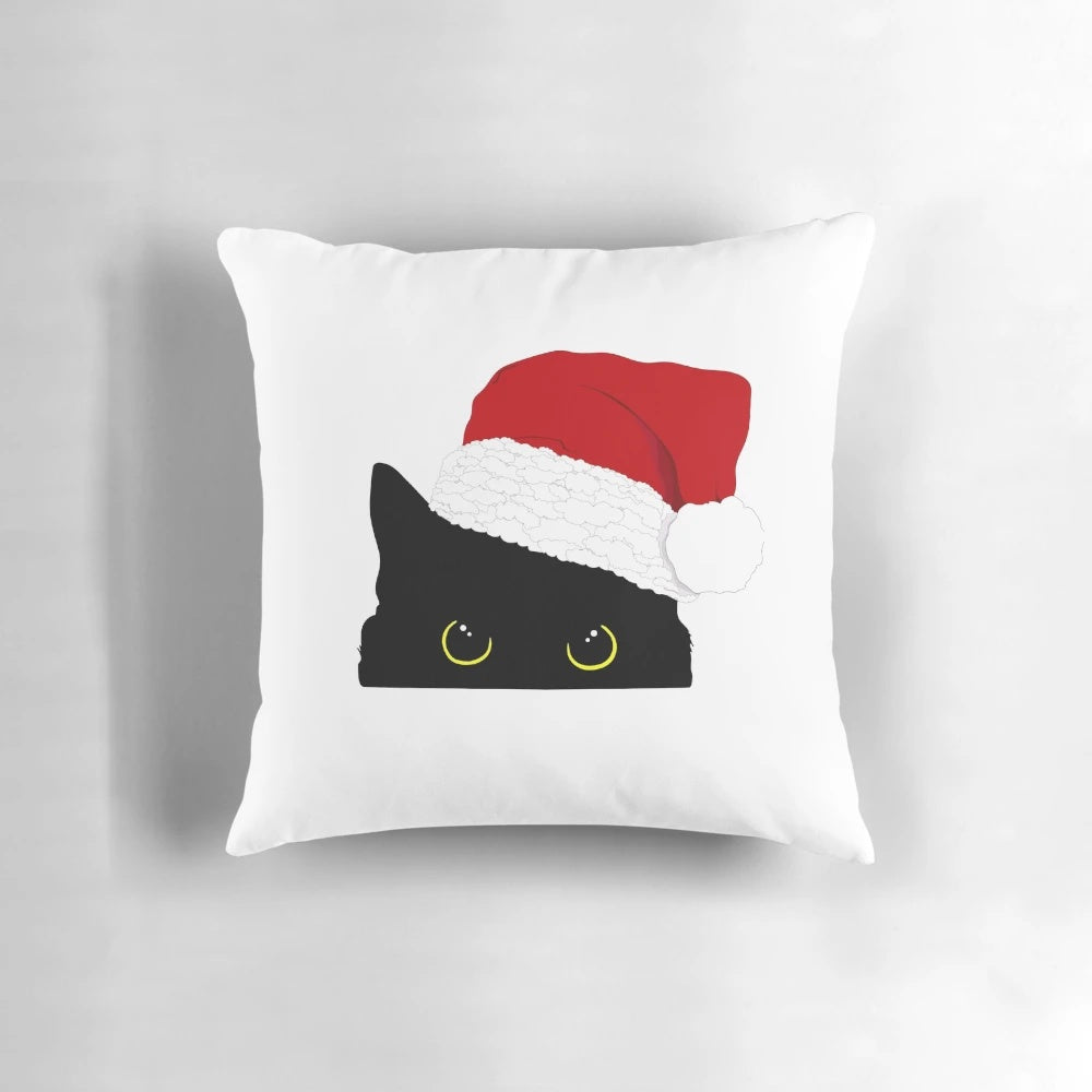 A cozy black cat peeking out from a Christmas pillow with a Santa Claus silhouette