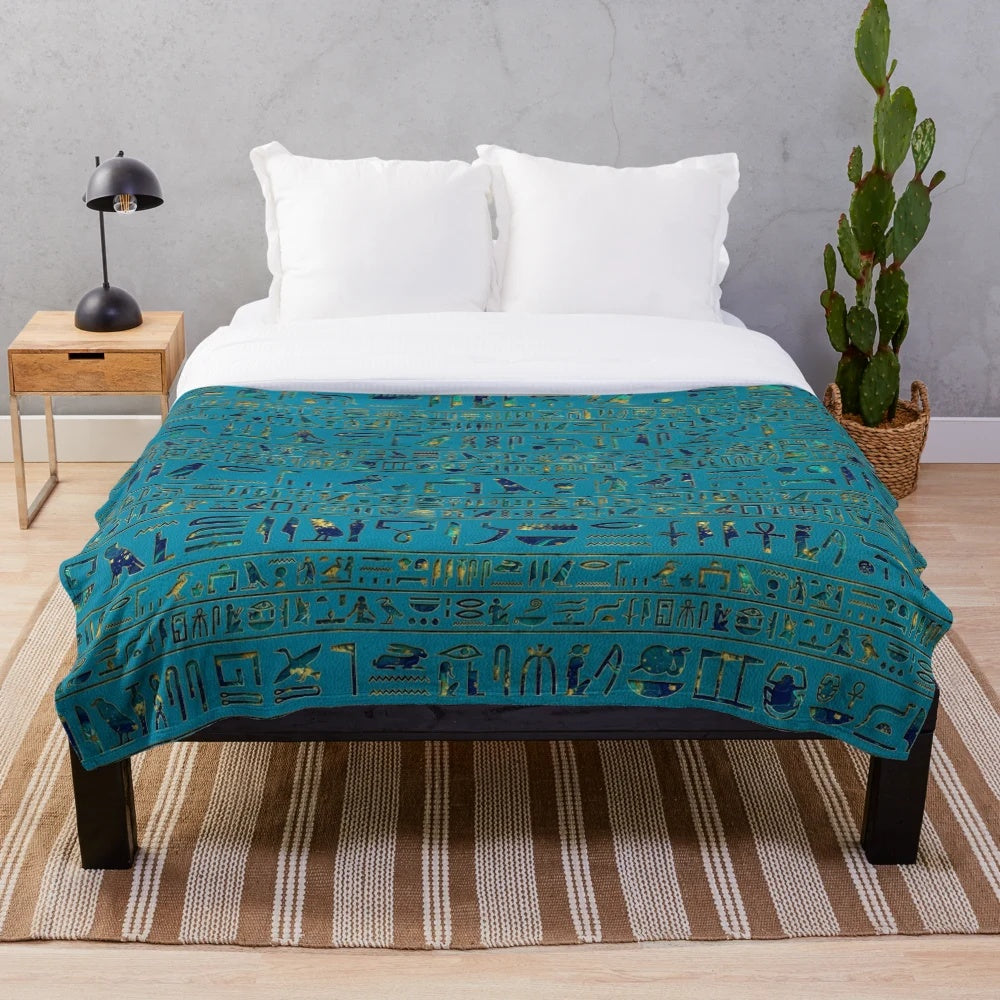 Plush blanket with intricate egyptian hieroglyphic design on teal leather-like texture