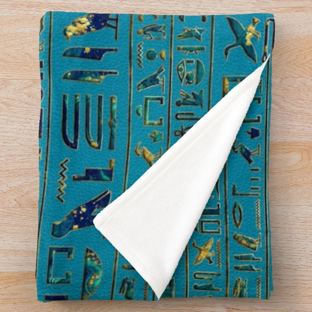 Plush blanket with intricate egyptian hieroglyphic design on teal leather-like texture