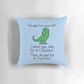 A plush, colorful dinosaur pillow with the text "Always Be Yourself, Unless You Can Be A Dinosaur"