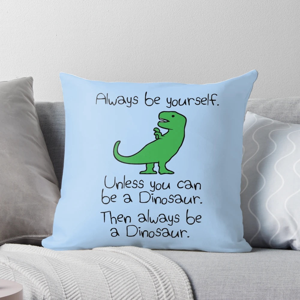 A plush, colorful dinosaur pillow with the text "Always Be Yourself, Unless You Can Be A Dinosaur"