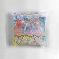 Vibrant abstract watercolor landscape design with radiating blue, green, and pink brush strokes and swirling yellow circles on a pillow.