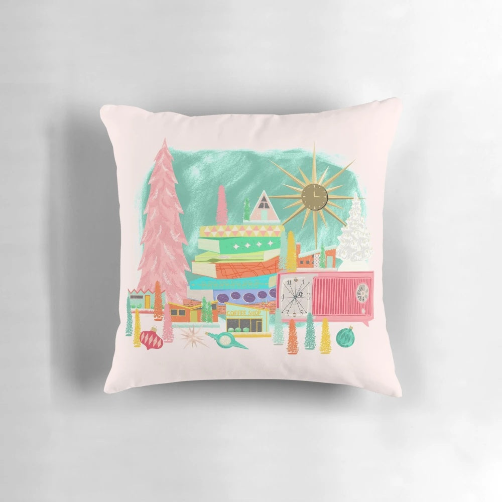 A mid century modern-inspired Christmas pillow featuring a vintage-style scene with a pink Christmas tree, starburst, and stack of books.