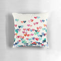A vibrant, hand-painted watercolor pillow featuring a heart pattern in shades of red, blue, and cream.