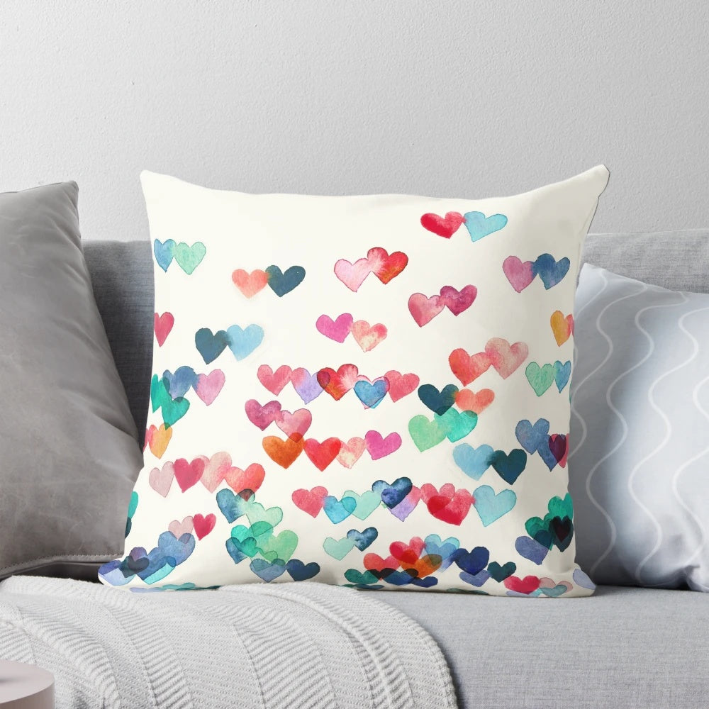 A vibrant, hand-painted watercolor pillow featuring a heart pattern in shades of red, blue, and cream.