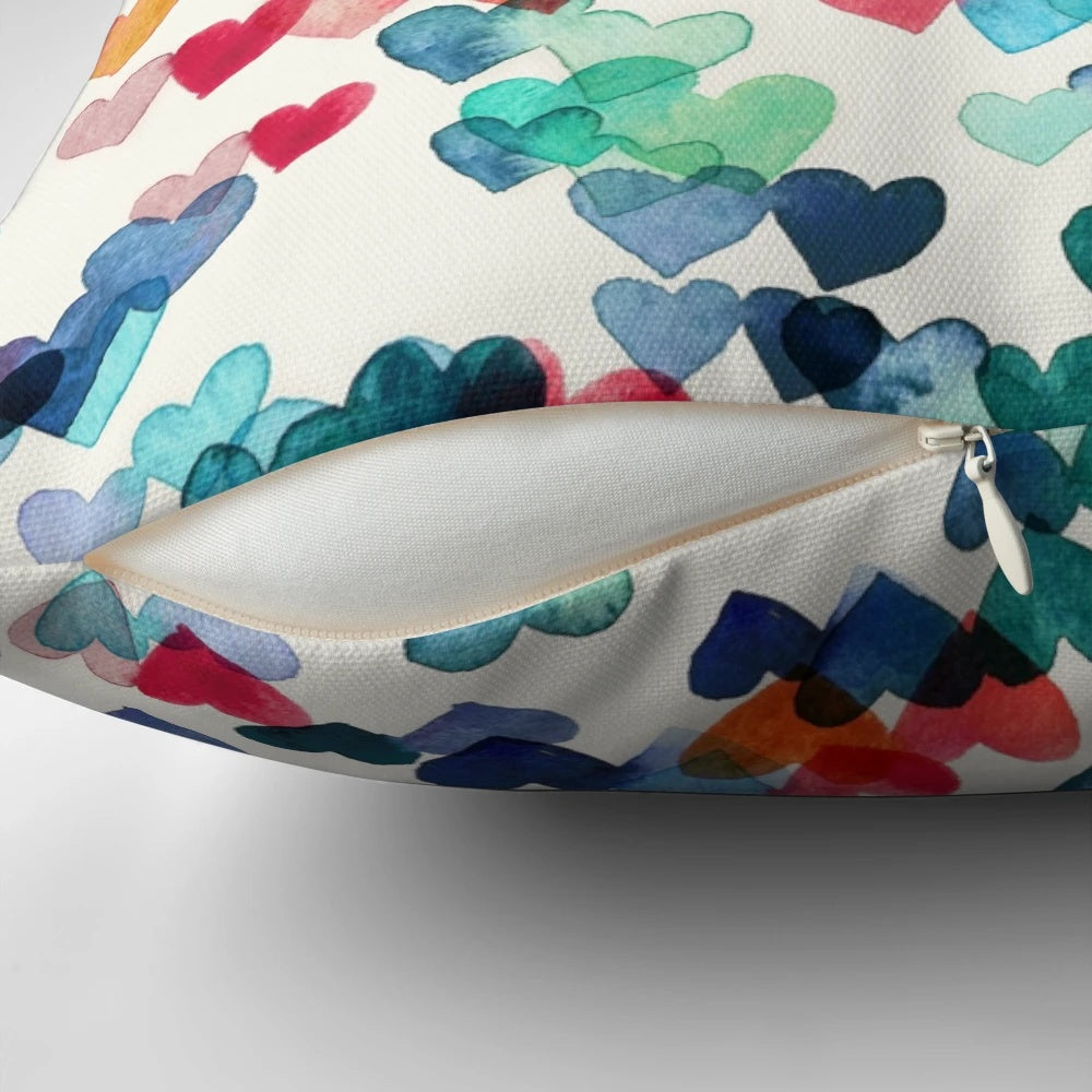 A vibrant, hand-painted watercolor pillow featuring a heart pattern in shades of red, blue, and cream.