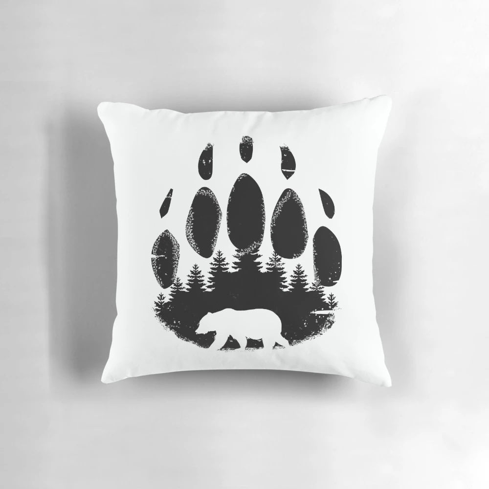 Black and white throw pillow featuring a bear paw print design against a forest landscape background.