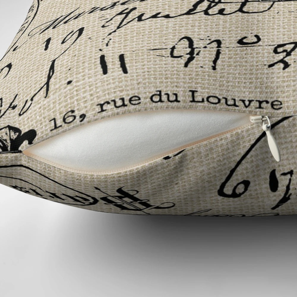 A neutral-colored decorative throw pillow with a handwritten French script design, perfect for adding a touch of vintage charm to any space.