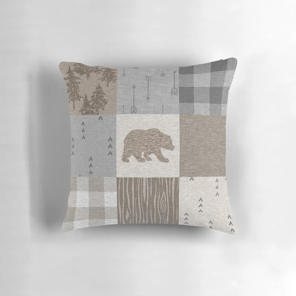A rustic patchwork pillow in neutral tones featuring a bear design, perfect for woodland and camping themed home decor.