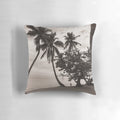Sepia-toned image of palm trees leaning over a tranquil beach with the ocean in the background