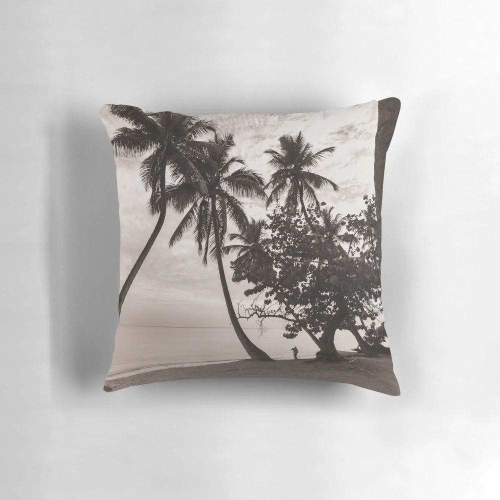 Sepia-toned image of palm trees leaning over a tranquil beach with the ocean in the background