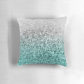 Closeup photo of a silver and teal pillow with a glittering, bokeh-like design, evoking a magical ocean scene.