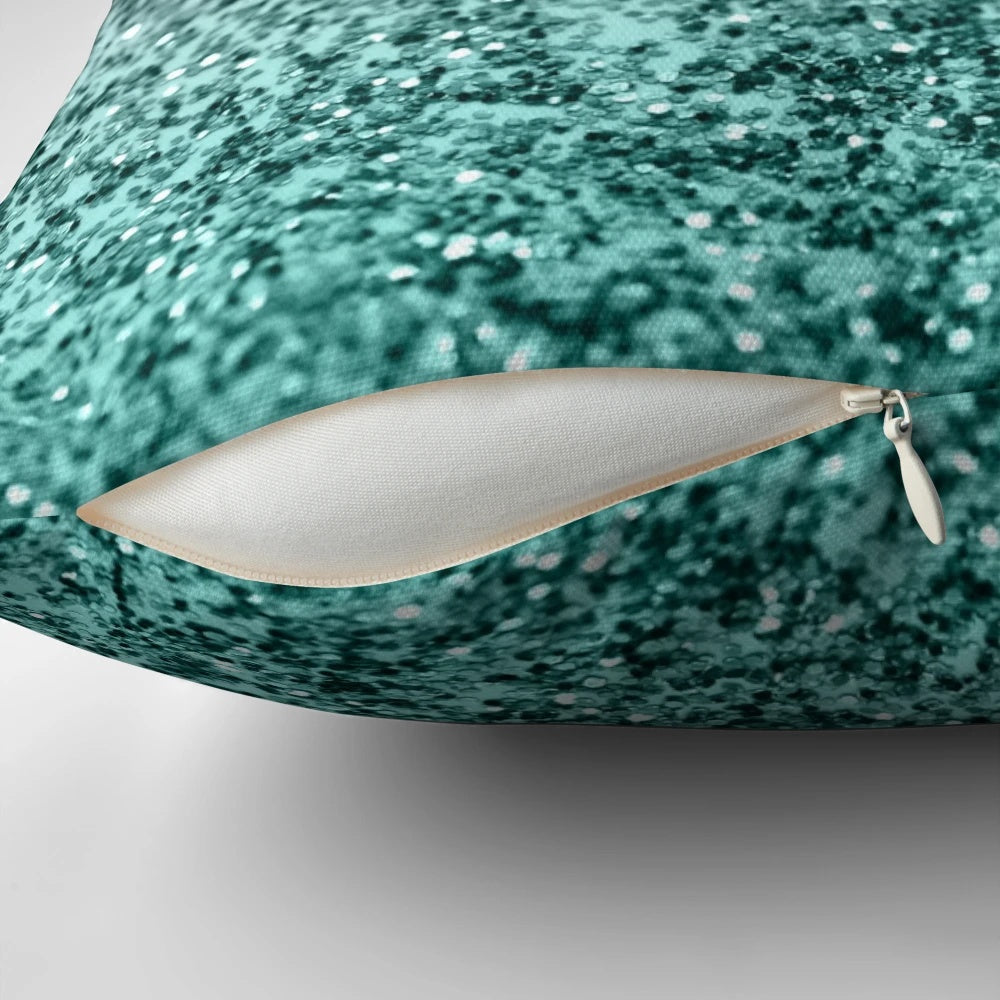 Closeup photo of a silver and teal pillow with a glittering, bokeh-like design, evoking a magical ocean scene.