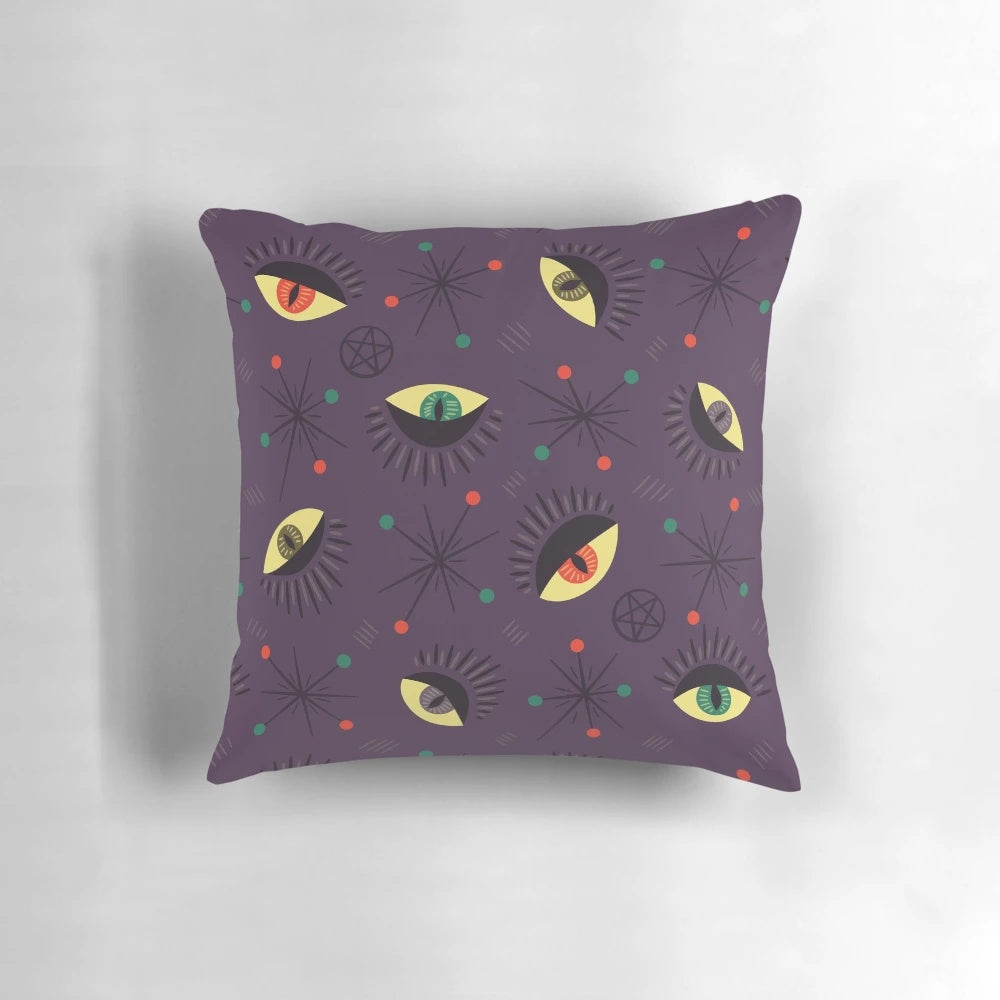 Decorative witch-themed pillow with a retro pattern featuring reptile and ghost eyes in shades of purple and black for a spooky, Halloween vibe.