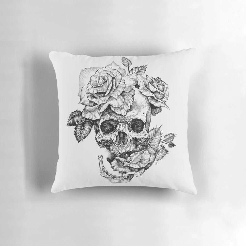 A black and white pen and ink drawing of a skull surrounded by roses on a decorative pillow.