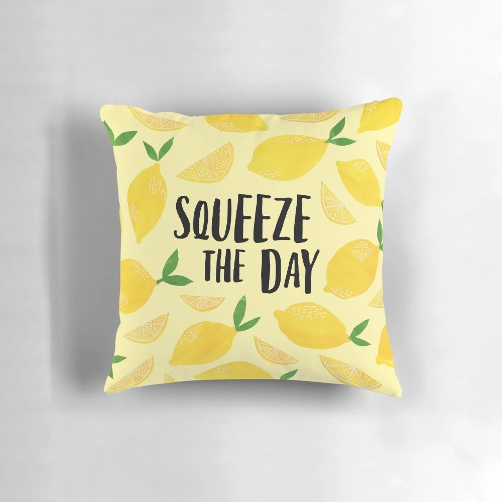A plush, square pillow featuring a lemon design with the text "Squeeze the Day" as a motivational and humorous home or office decor accessory.