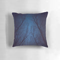 A decorative throw pillow featuring a print of a night sky with a silhouette of trees and a galaxy of stars in shades of indigo blue.