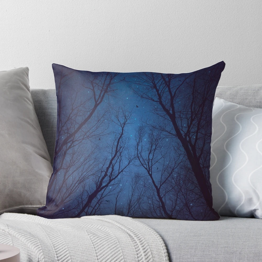 A decorative throw pillow featuring a print of a night sky with a silhouette of trees and a galaxy of stars in shades of indigo blue.