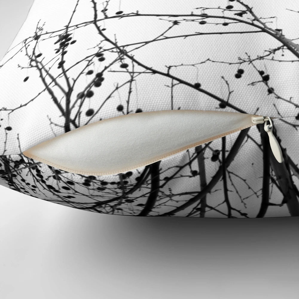 A decorative black and white pillow featuring an abstract design of bare tree branches against a neutral background, capturing the beauty of the autumn season.