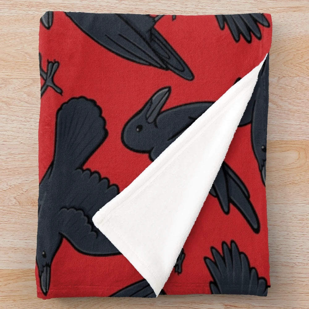 A plush blanket featuring a repeating pattern of crows or ravens in black and red