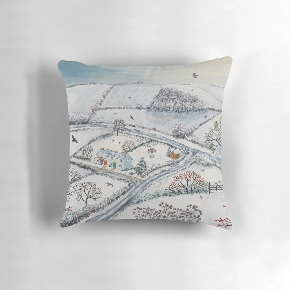 A cozy pillow featuring a winter landscape with snowy hills, houses, and birds in the snow.