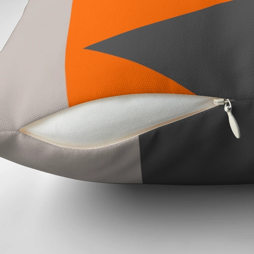 Close-up of a decorative throw pillow featuring a modern, minimalist pattern of orange and grey triangles.