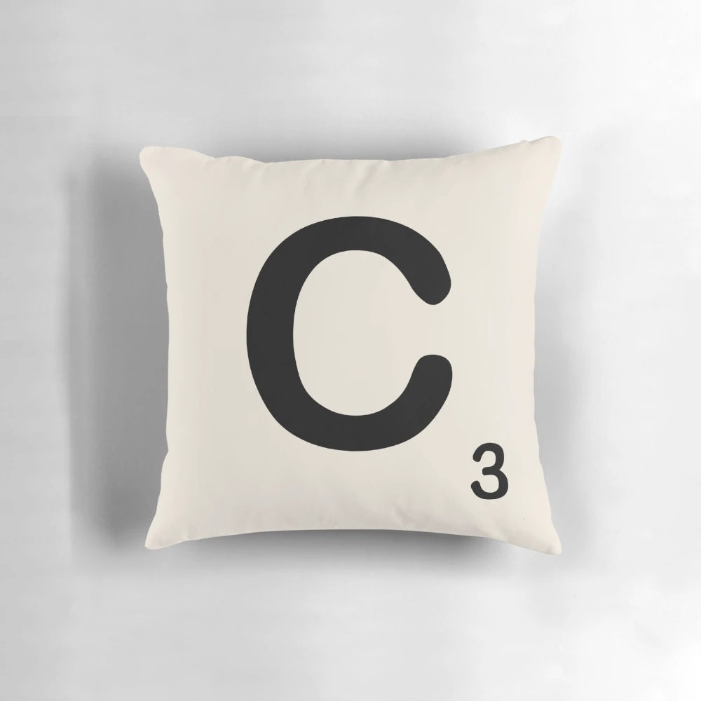A decorative throw pillow featuring a Scrabble-style letter 'C' in a bold, retro typeface.