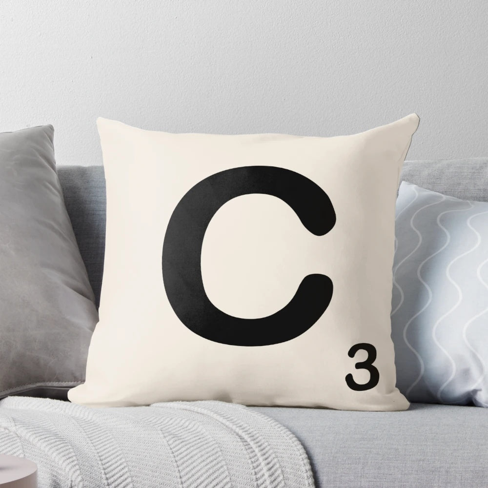A decorative throw pillow featuring a Scrabble-style letter 'C' in a bold, retro typeface.