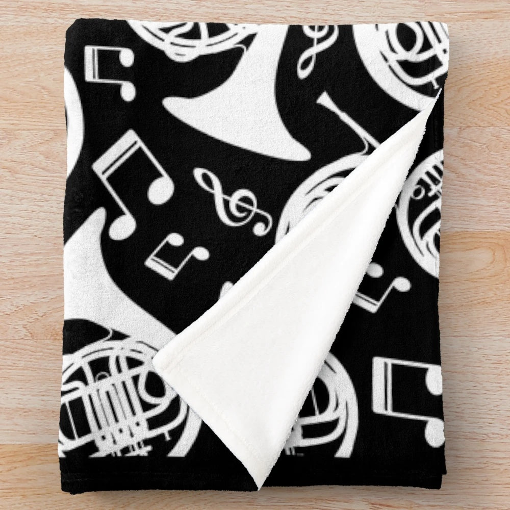 White plush blanket featuring a pattern of french horns and music notes