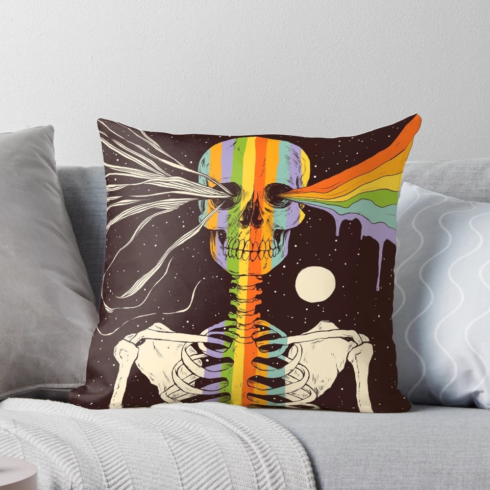 A decorative pillow with a dark, surreal design featuring a skull, skeleton, and celestial elements like stars, moons, and rainbows against a dark background.
