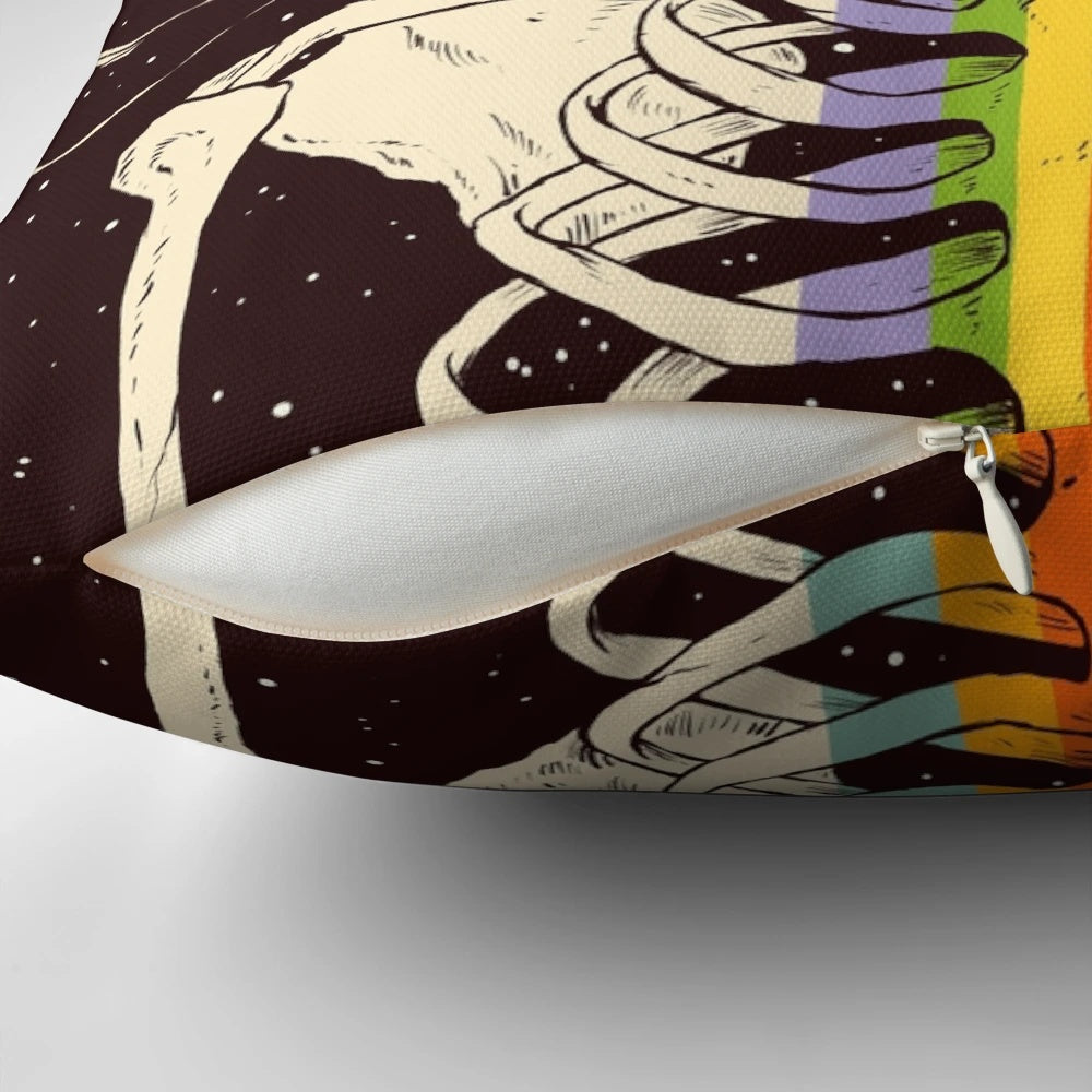 A decorative pillow with a dark, surreal design featuring a skull, skeleton, and celestial elements like stars, moons, and rainbows against a dark background.