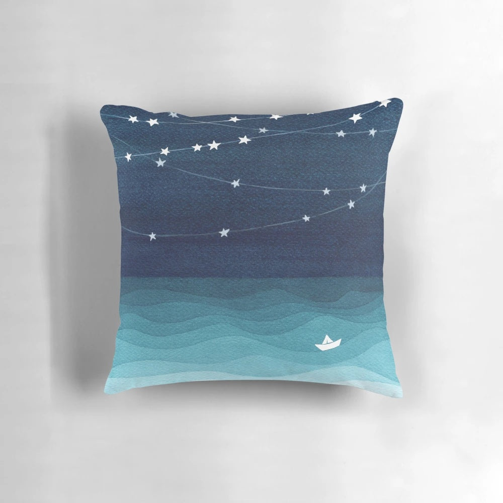 Teal and white pillow with a garland of stars design, depicting a paper boat sailing on the ocean.