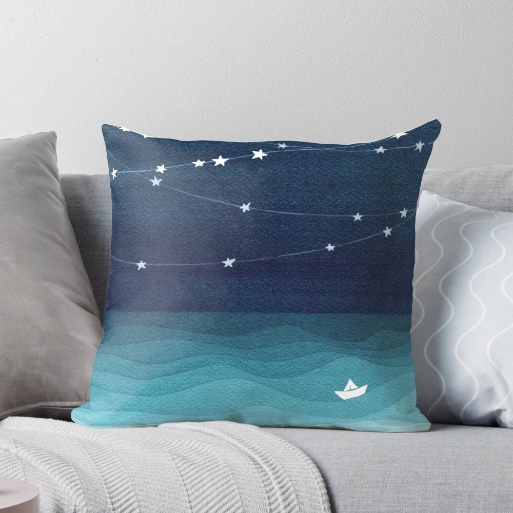 Teal and white pillow with a garland of stars design, depicting a paper boat sailing on the ocean.
