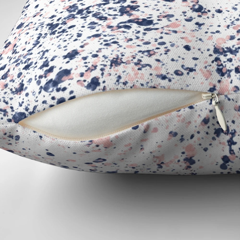 Navy blue and blush pink abstract ink spatter pattern on a white decorative pillow