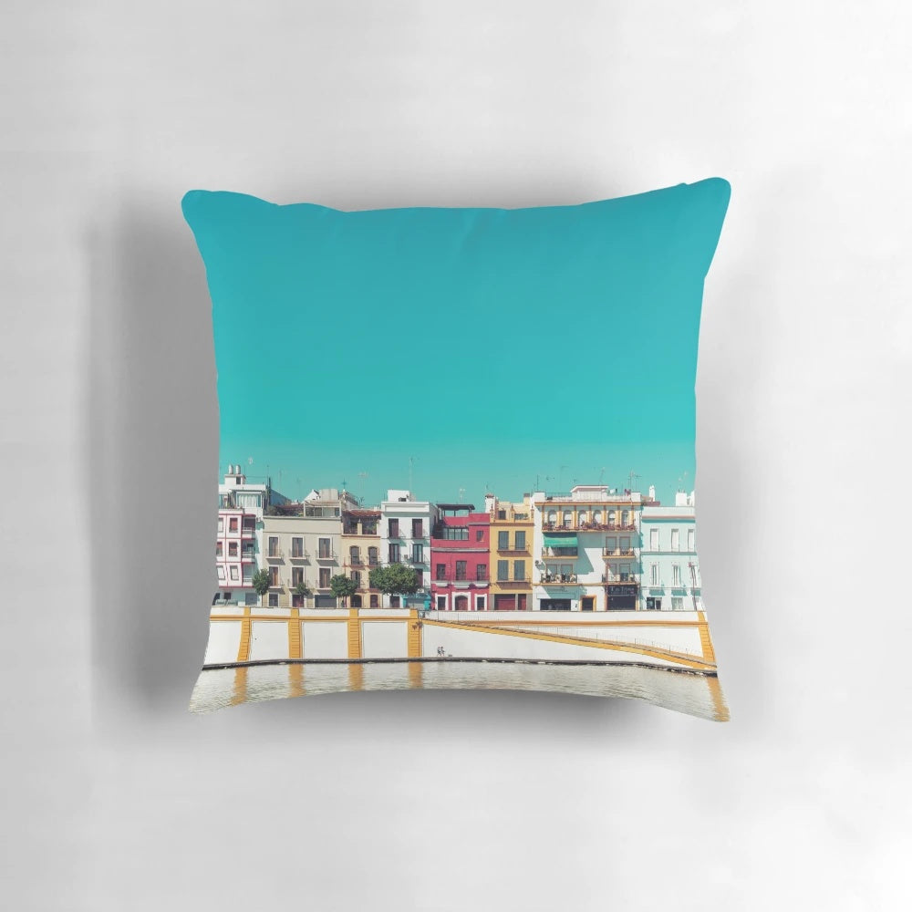 A decorative pillow featuring a stunning cityscape of Triana, Seville, Spain with a blue sky, trees, and houses.
