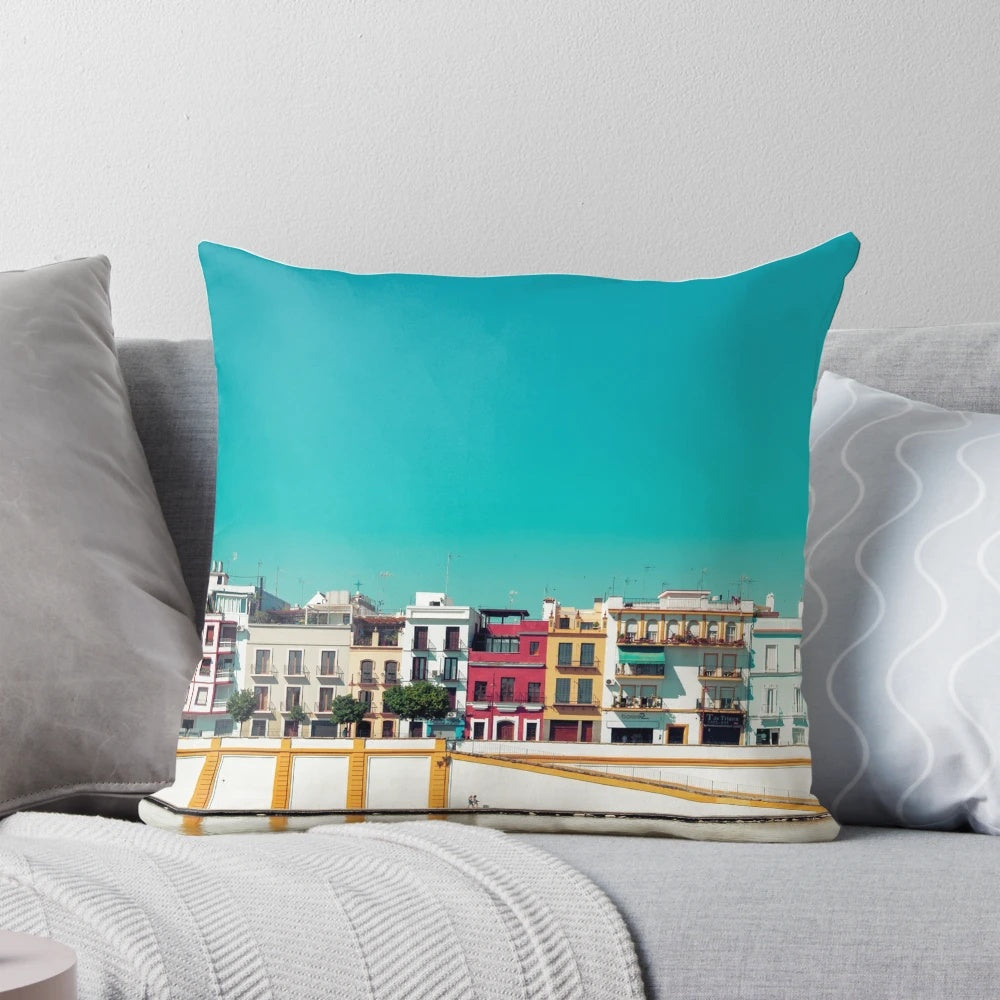 A decorative pillow featuring a stunning cityscape of Triana, Seville, Spain with a blue sky, trees, and houses.