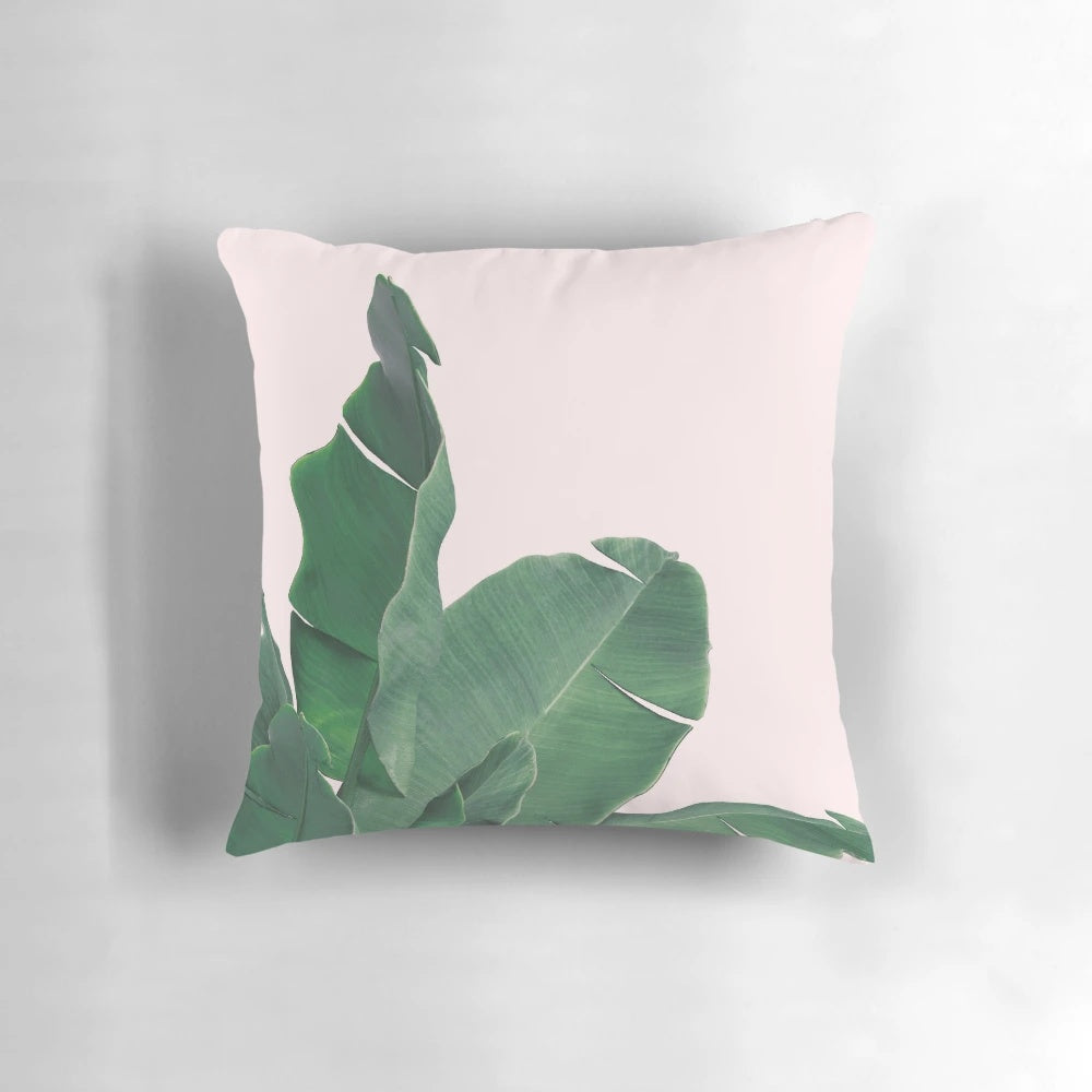 Tropical pillow featuring vibrant banana leaves and lush botanical foliage on a pink background.