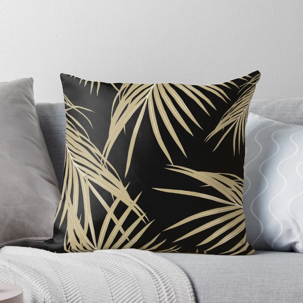 A gold and black tropical palm leaf print pillow, featuring a collage of lush palm fronds and foliage.