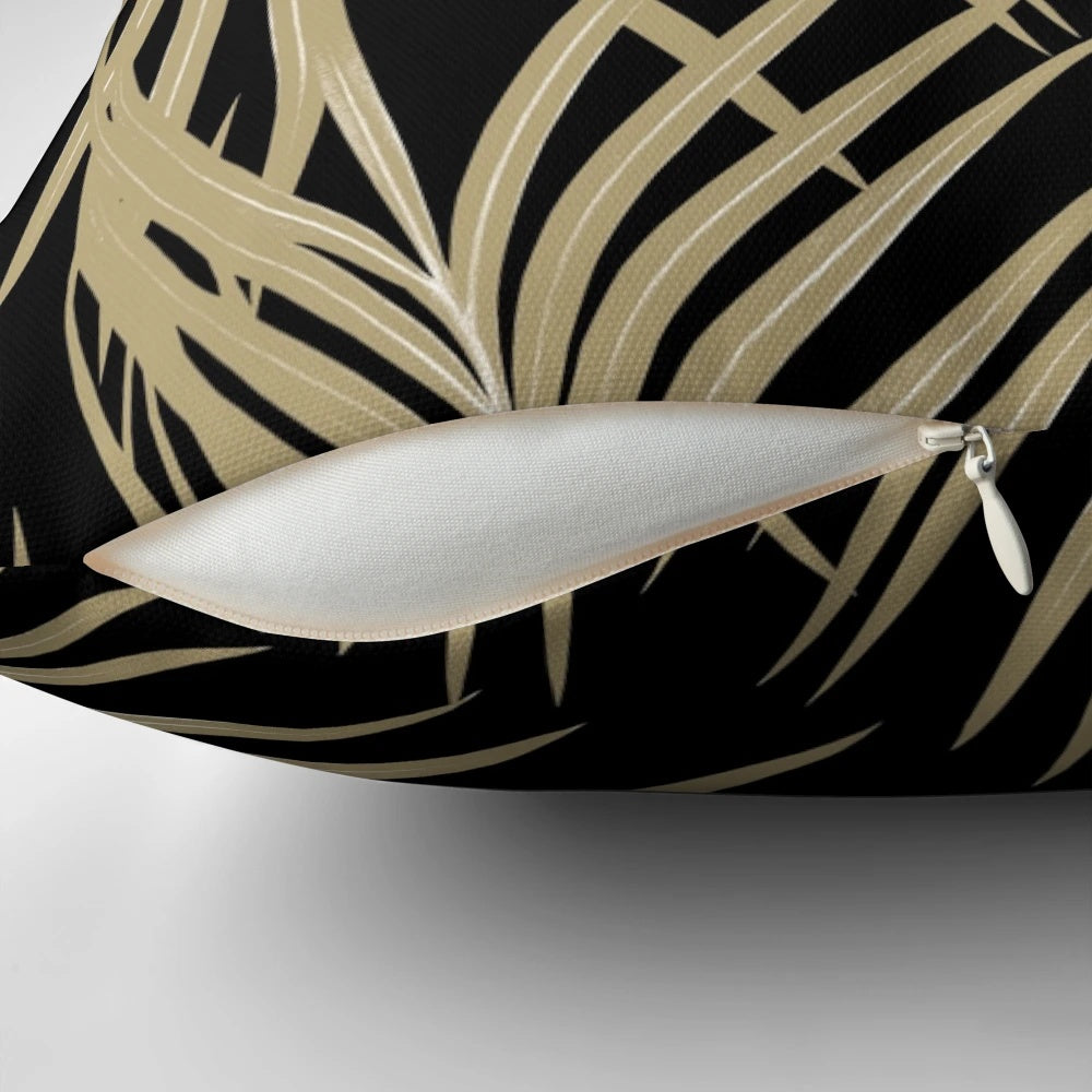 A gold and black tropical palm leaf print pillow, featuring a collage of lush palm fronds and foliage.