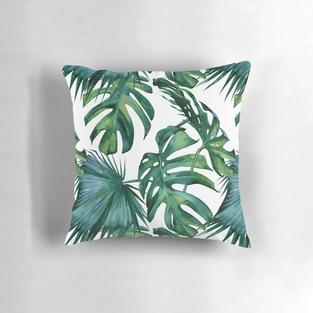 Decorative pillow featuring tropical monstera and palm leaves on a white background