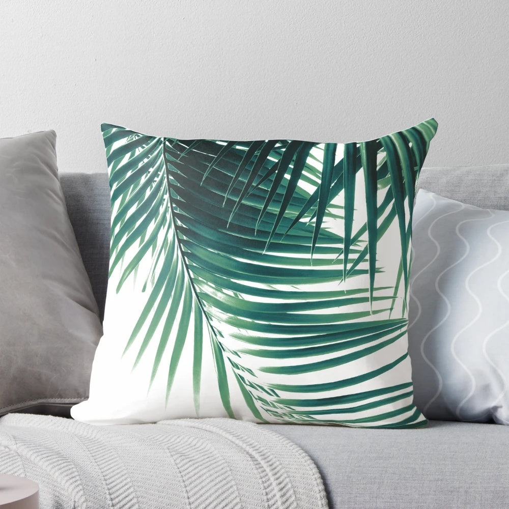 Decorative pillow featuring a digital art design of tropical palm leaves in shades of green on a white background.