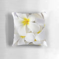 A throw pillow featuring a high-key close-up photograph of white plumeria or frangipani tropical flowers