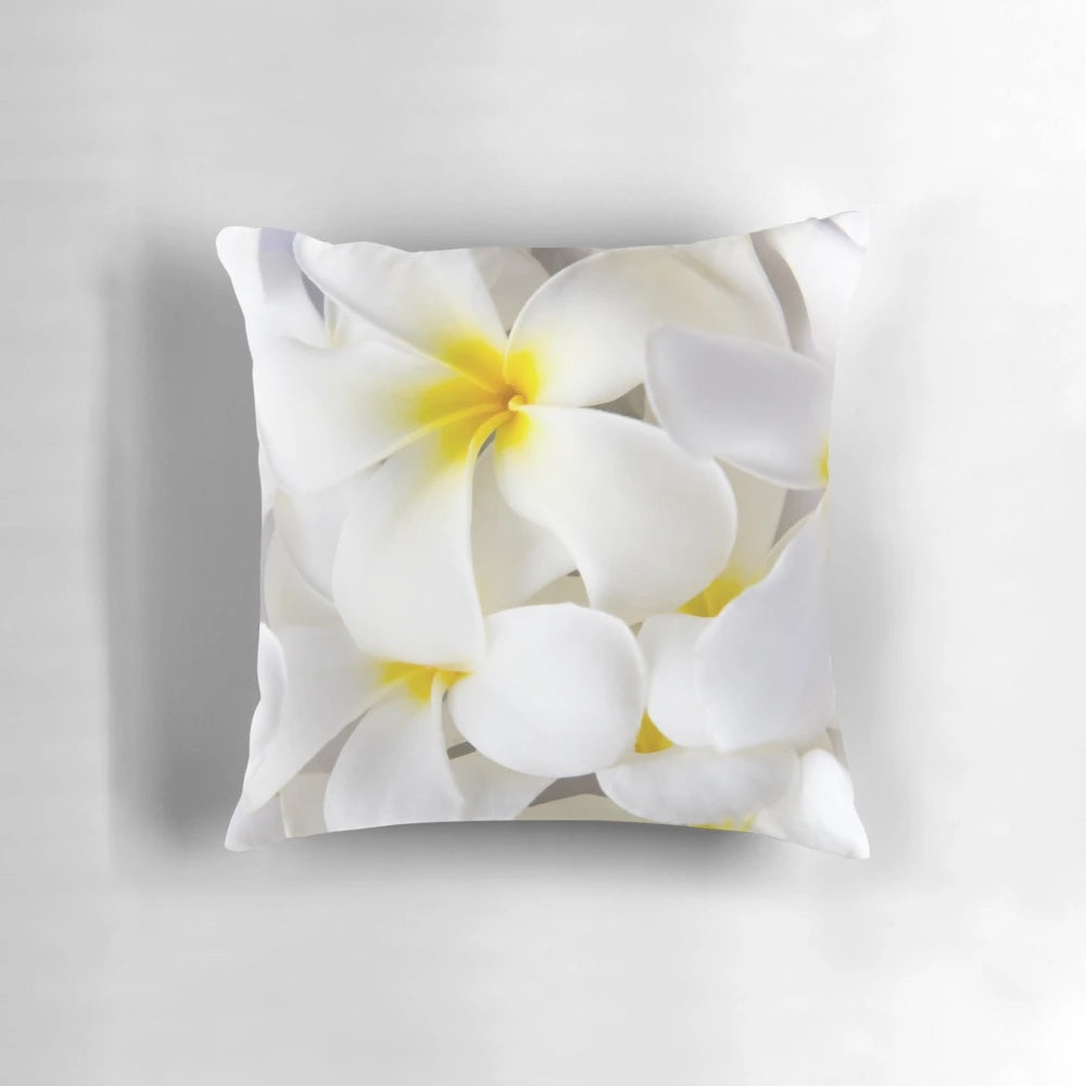 A throw pillow featuring a high-key close-up photograph of white plumeria or frangipani tropical flowers