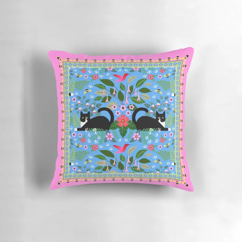 Tuxedo cat resting on a pillow with a hummingbird design